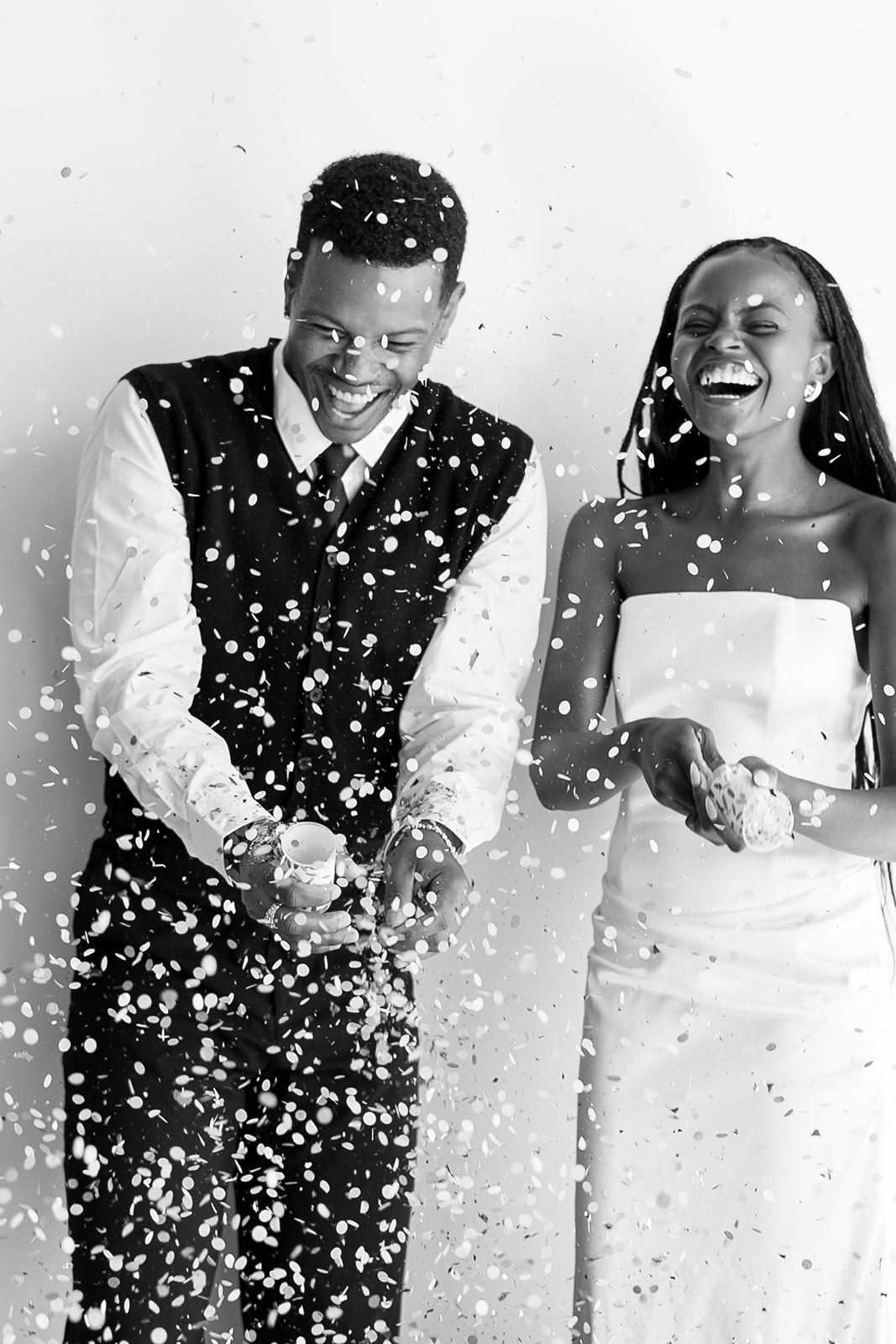 Black-and-white shot of a laughing couple in a shower of confetti, she in a strapless white dress